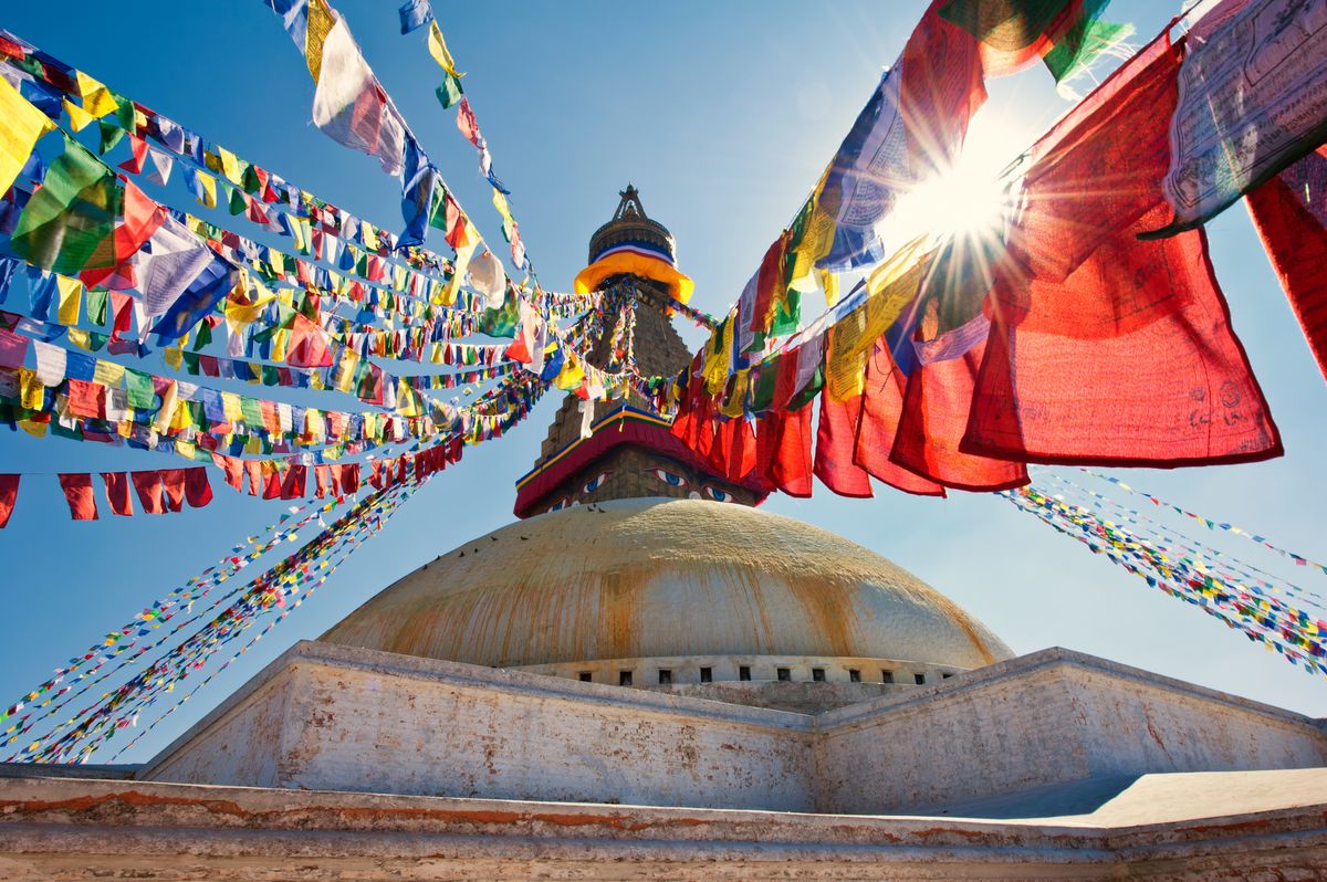 The center of the image shows the Boudhanath Stupa in Nepal. Around it hang many Tibetan prayer flags, © Adobe Stock, Photo: Emanuel