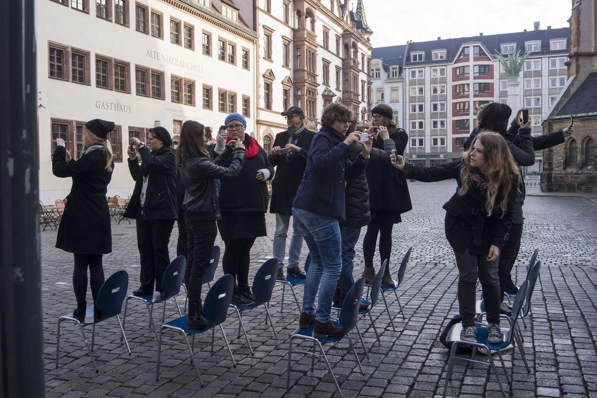 zur Vergrößerungsansicht des Bildes: Personen stehen auf blauen Stühlen neben der Nikolaikirche und fotografieren sich gegenseitig mit ihren Smartphones