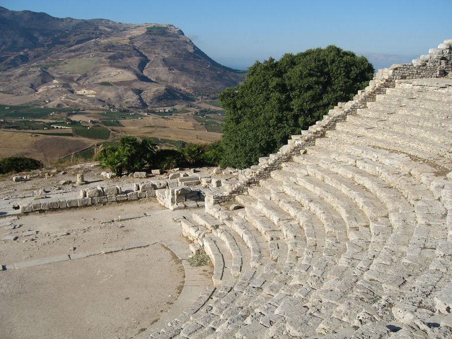 Überreste einer antiken Amphitheateranlage aus hellem Stein, im Hintergrund Berge