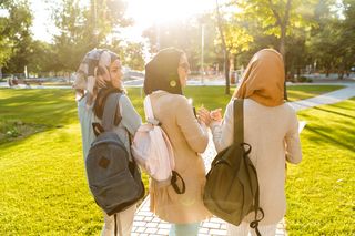 Drei Studentinnen, die ein Kopftuch tragen, laufen einen Weg mit Büchern in der Hand entlang.