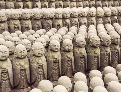 In mehreren Reihen sind kleine Steinstatuen buddhistischer Mönche hintereinander aufgestellt.