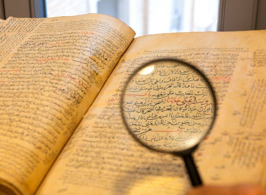 zur Vergrößerungsansicht des Bildes: Eine Lupe wird auf ein arabisches Buch gehalten