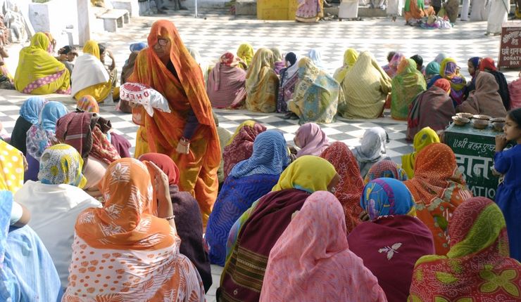 Frauen sitzen auf einem gefliestem Boden in farbenfrohen Saris