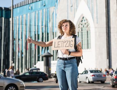 Ein Mädchen trampt mit einem Schild nach Leipzig