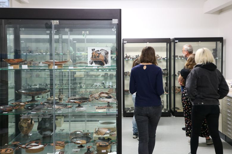 Seminargruppe steht im Depot des Antikenmuseums mit Originalobjekten in Glasvitrinen