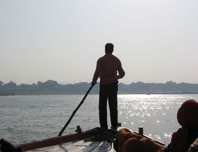 Silhouette des Bootsführers mit einer Stange auf der Spitze des Bootes stehend, dahinter der Fluss und die Stadt am Ufer im Gegenlicht, Bootsfahrt auf dem Fluss Ganges, Varanasi, Indien, 2013, Foto: Johanna Buß
