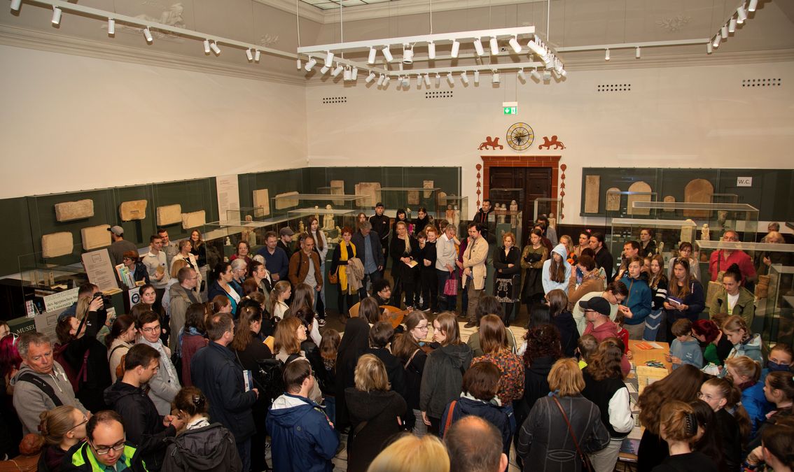 zur Vergrößerungsansicht des Bildes: Halle voller Menschen, in der Mitte eine Frau mit Laute