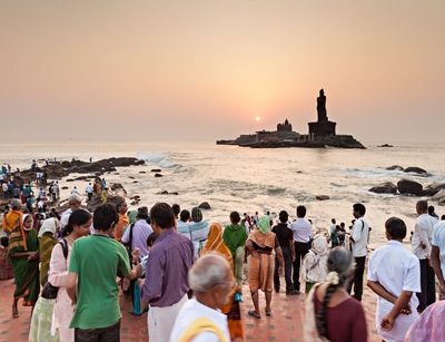 Zahlreiche Menschen stehen am Strand und richten ihren Blick auf eine kleine Insel mit einer großen Statue