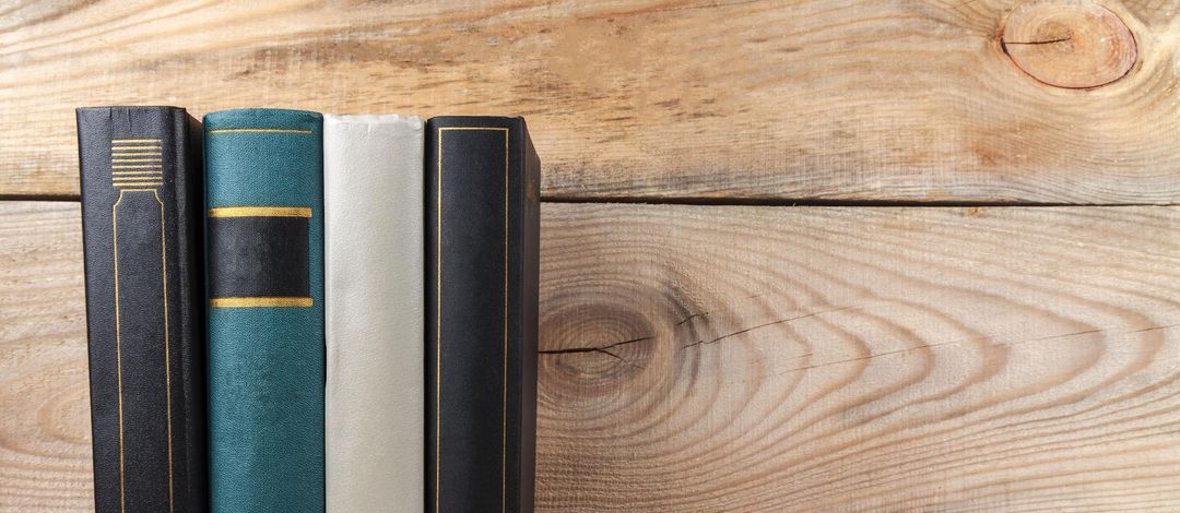 Vier Bücher stehen aufrecht vor einer Holzwand.