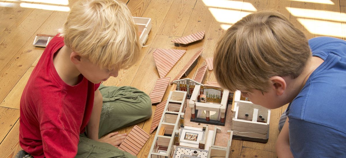 Zwei Jungs spielen mit einem Holzmodell einer römischen Villa.