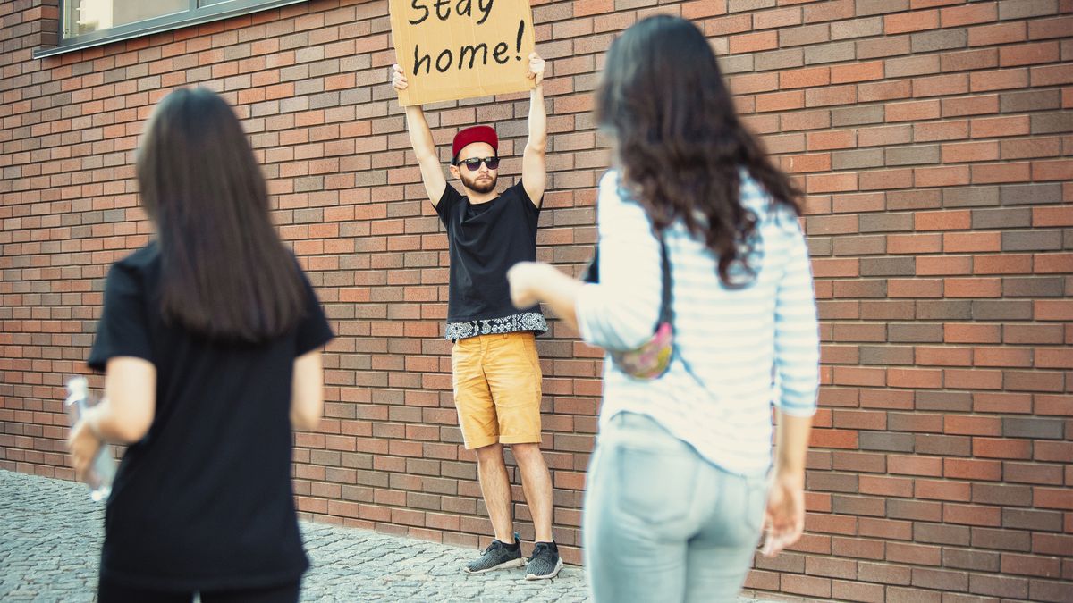 Ein Mann hält auf der Straße ein Schild mit der Aufschrift "Stay Home"