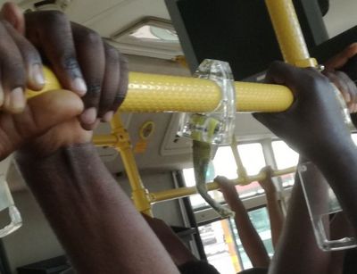 Hands holding on to a yellow handrail on a bus in Dar es Salaam.
