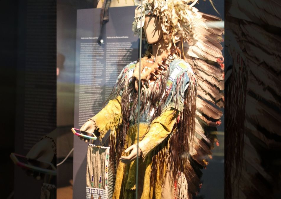 Eine Figur in einem Museum im traditionellen Kostüm der ersten Einwohner Amerikas hält ein Handy in der Hand