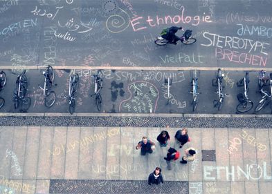 Auf der Straße sind mit Kreide Begriffe gemalt, Studierende stehen daneben, Institut für Ethnologie Leipzig