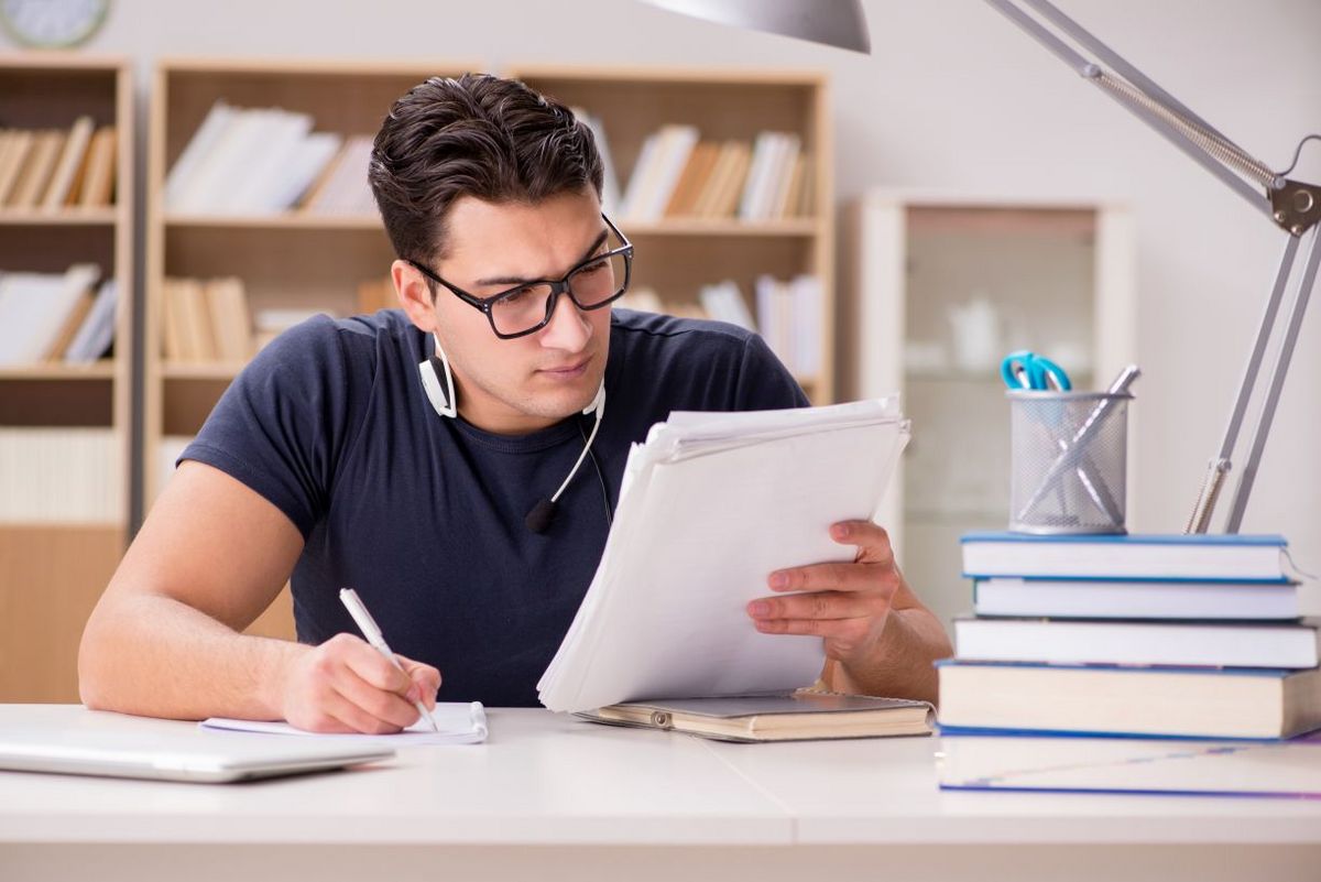 Ein Student sitzt an seinem Schreibtisch und studiert konzentriert seine Unterlagen.