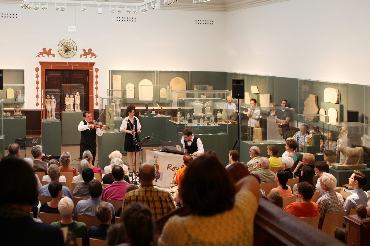 zur Vergrößerungsansicht des Bildes: Band mit Instrumenten und Sängerin, davor sitzendes Publikum in der Museumshalle