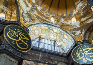 Blick in die mit Ornamenten und goldenen Schriftzeichen versehene, prächtige Kuppel der Hagia Sophia.