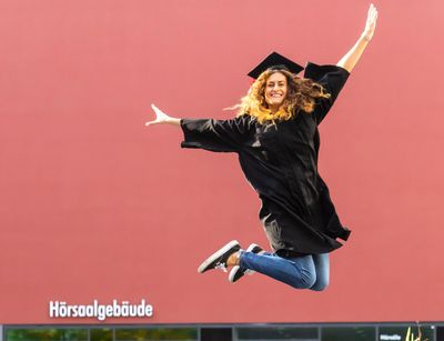 Eine Studentin im schwarzen Talar springt in die Luft vor Freude, Foto: Christian Hüller