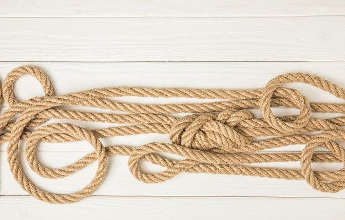 Ein Seil liegt in Schlingen und in Knoten vor einem hellen Hintergrund