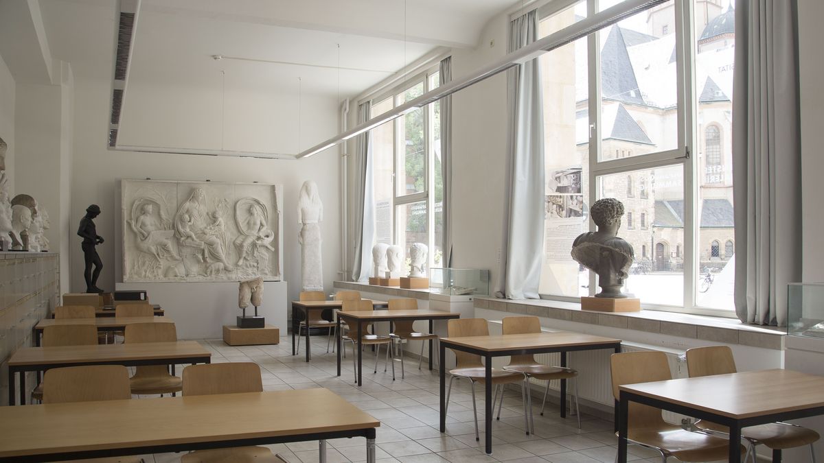 Der Studiensaal in der Ritterstraße 14, im Raum stehen Tische und Stühle als Plätze für Studierende, an den Wänden des Raumes sind Abgüsse antiker Skulpturen ausgestellt, auf dem Fensterbänken sind weitere Gipsabgüsse antiker Skulpturen platziert, durch die Fenster ist zudem im Hintergrund die Nikolaikirche zu erkennen
