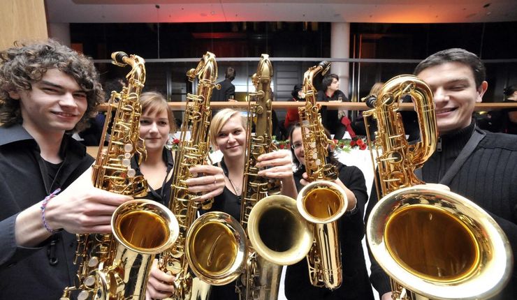 Foto: Fünf Musiker und Musikerinnen in schwarz gekleidet halten ihr Saxophon in die Kamera
