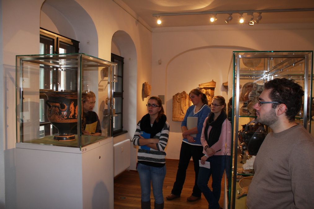 Studierende stehen im Antikenmuseum vor Vitrinen und betrachten antike Gefäße.