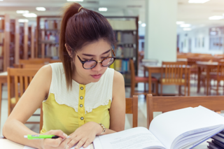 Eine Studentin sitzt in einer hellen Bibliothek und macht sich Notizen beim Lesen.