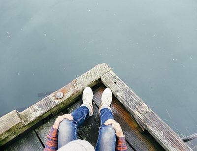 Ein von oben fotografiert Person sitzt auf dem Bootssteg mit Blick zum Wasser.