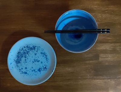 Zwei blaue Reisschalen stehen auf einem Holztisch. Auf einer Schale liegen Essstäbchen.