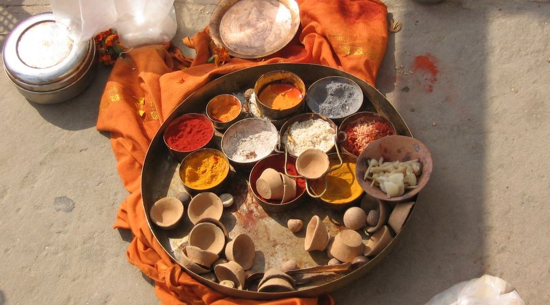 Metallschalen mit verschiedenfarbigen Pulvern und Gewürzen auf einem Holztablett, das auf einem orangefarbenen Tuch auf dem Steinfußboden steht, das sind Untensilien für das hinduistische Totenritual Shraddha, Varanasi, Indien, 2011, Foto: Johanna Buß