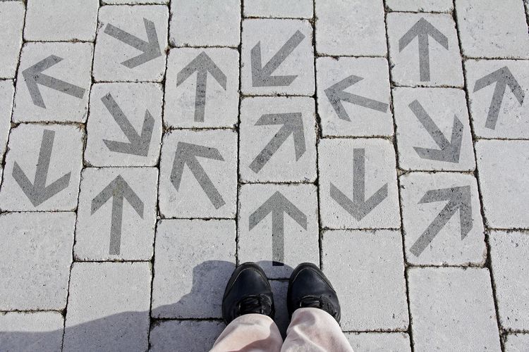 A Person standing in front of arrows on the floor that are pointing in different directions