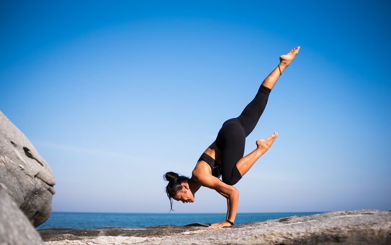 Foto einer Frau, die auf einem Felsen vor einem Meer die Yoga-Stellung einbeinige Krähe ausführt, © Pixabay, Foto: StockSnap