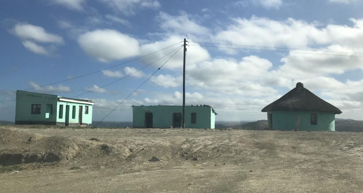 Ein Gehöft im ländlichen Südafrika, bestehend au seiner runden Hütte und zwei rechteckigen Gebäuden, die alle über Elektrizitätskabel miteinander verbunden sind.