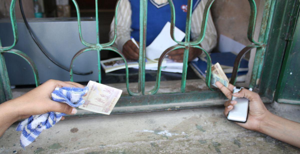 enlarge the image: two hands pass banknotes into a barred ticket window at Bara Imambara Palace, Lucknow, India, 2013, photo by Ira Sarma.