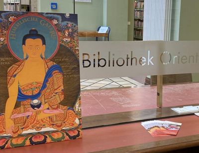 Illustrated book with Buddhist art on a table in the entrance area next to the lettering Bibliothek Orientwissenschaften, 2020, Photo: Franz Xaver Erhard