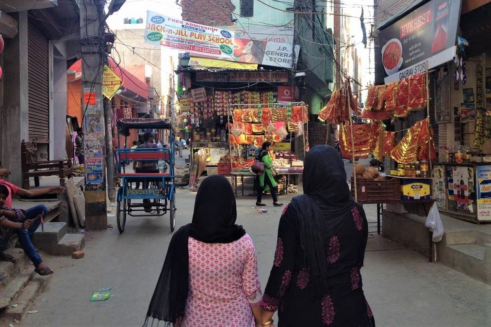 Two Indian women walk through a narrow street with shops