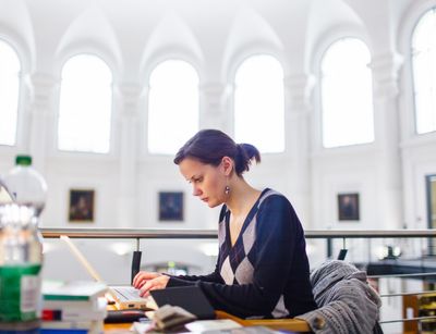 Foto: Eine Studentin sitzt an einem Arbeitsplatz in der Bibliotheca Albertina und tippt etwas in den Laptop